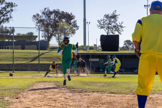 Male sports player helmeted sprinting toward home plate on ball in play, trying to score
