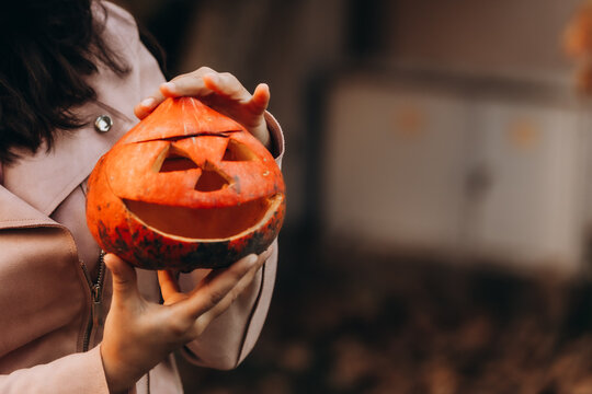 Close up of girl holding carved pumpkin lantern outdoors during Halloween celebration with warm autumn mood spooky season decor trick or treat tradition playful fall holiday atmosphere seasonal scene