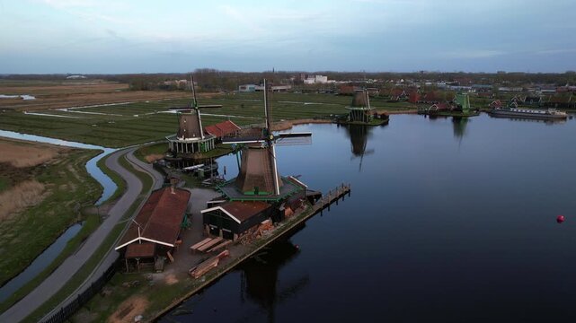 Historic traditional windmills of Zaanse Schans at sunset in Netherlands aerial view. Evening twilight sky, green fields, and rural canals of Holland.