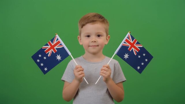 A young boy holding two small Australian flags isolated on a green screen chroma key background.