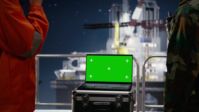Chroma key laptop and walkie talkie used by army unit on drilling rig to enforce maritime embargo protocol with green screen laptop mockup.