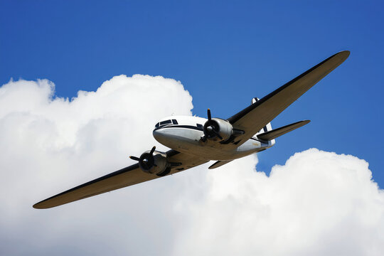 Classic Douglas DC-3 plane flies through blue sky with clouds. This twin-engine propeller aircraft has a vintage look and represents aviation history and travel.