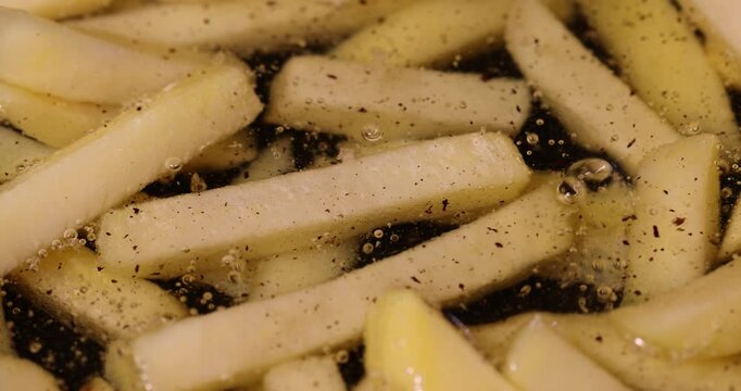 overcooked French fries in hot sunflower oil during frying in a frying pan, delicious fast food yellow thawed and fried French fries in hot oil