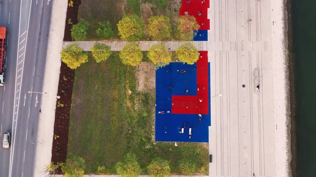 Aerial drone shot of colorful sports ground beside Tagus riverside promenade in Lisbon Portugal. Overhead city view with people exercising near waterfront urban landscape