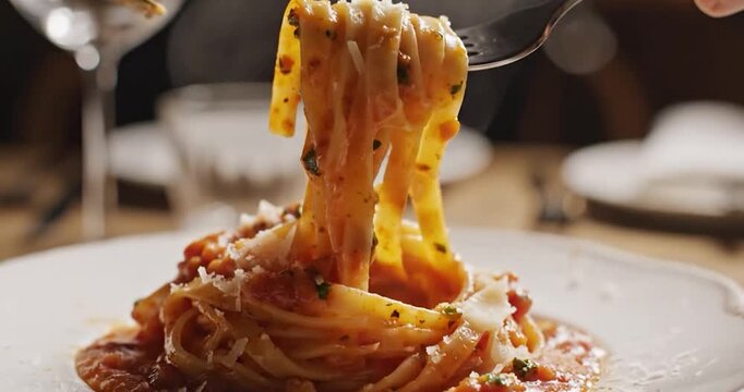 Person using a fork and knife to twirl fresh pasta with tomato sauce