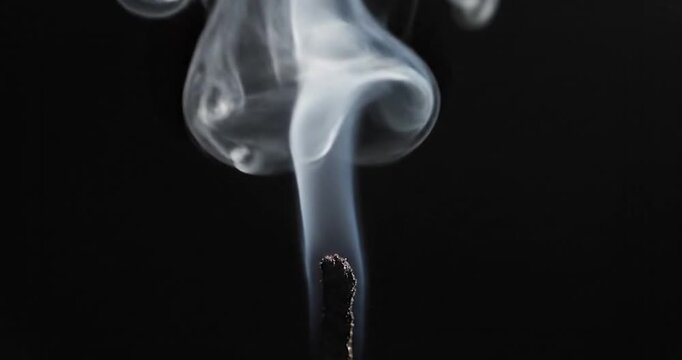 Thin wisps of white smoke rising from a burning match on black background