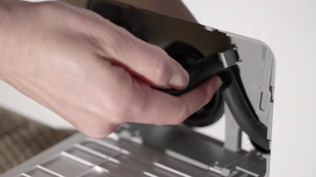Person draining water from washing machine filter. Person opening the small door of a washing machine to pull out the drain hose, unplugging it, and letting the excess water flow out into a tray