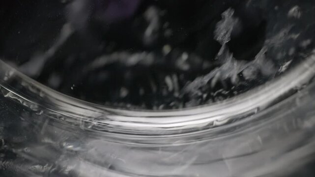 Washing machine drum spinning with clothes and soapy water. Close-up view of a washing machine drum in motion with dark and colored clothes tumbling in soapy water, showcasing the cleaning process