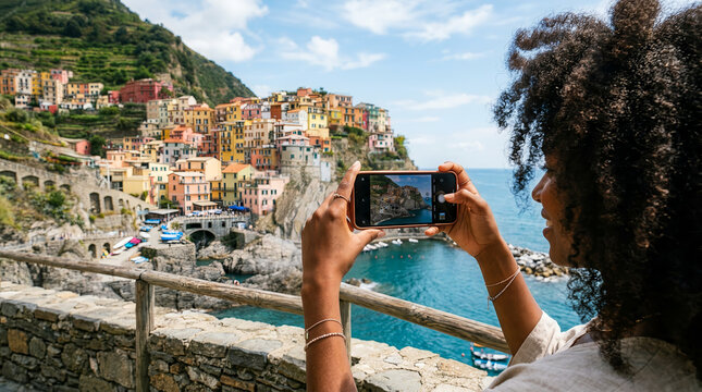 African-American woman capturing a photo of Manarola, Cinque Terre, Italy, with her smartphone.