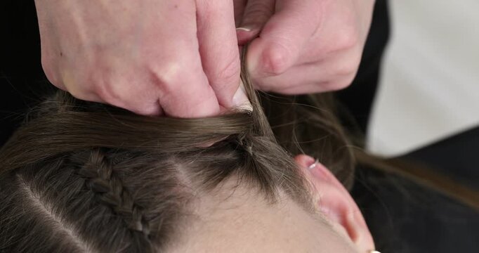Hairstylist braiding teenage girl's hair indoors, closeup