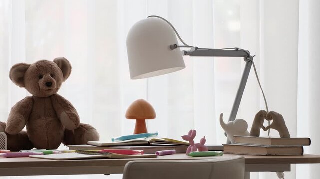 Stylish workplace with lamp, decor and stationery on table near window in child's room, camera moving left. Interior design