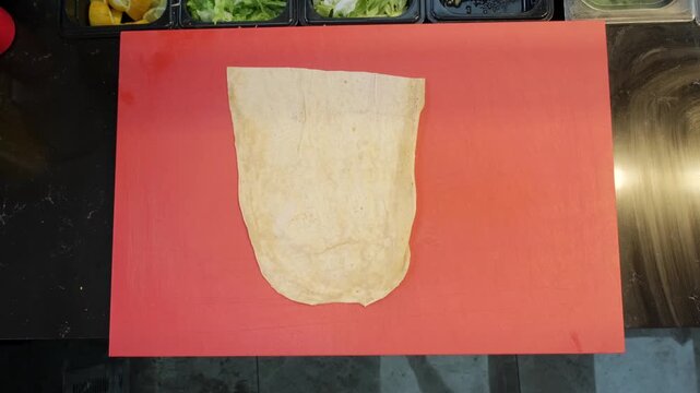 A direct overhead top down video of an authentic chef placing a fresh lavash flatbread onto the counter, getting ready to prepare a traditional spicy Turkish cig kofte wrap.