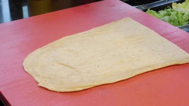 A close up video shot from a forty five degree angle showing an open lavash bread spread on the counter, ready for the chef to prepare a traditional spicy Turkish cig kofte wrap.