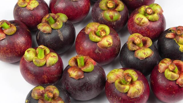 A close-up loop video of ripe purple mangosteen fruits rotating on a clean white surface.