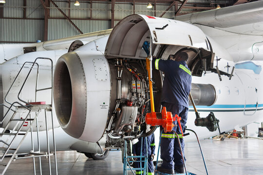 Aircraft mechanics performing maintenance on turboprop jet engine in hangar