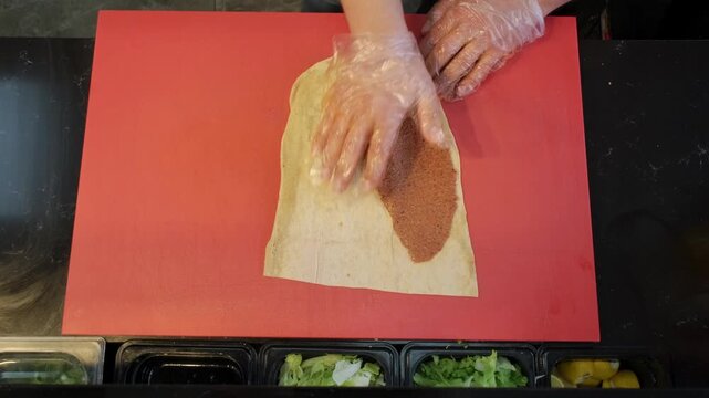 A direct ninety degree overhead close up video of a master chef smoothly spreading fresh spicy cig kofte paste onto a soft lavash flatbread, crafting an authentic Turkish wrap.
