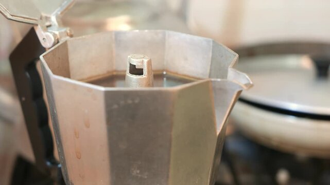 Close-up of a steaming moka pot on the stove. Hot espresso. Black coffee. Steam rising from a coffee maker. An Italian coffee maker on a stove. POV: preparing coffee. Making coffee in the kitchen
