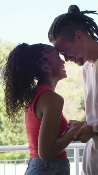 Vertical video: Holding hands couple leaning heads close on balcony showing love in red tank