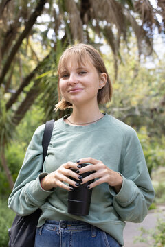 Female in twenties holding black travel mug with both hands showing backpack strap on park path