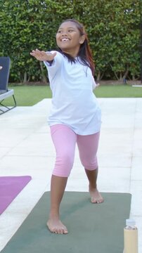 Vertical video: Child in pink leggings flowing lunge to reach on patio after coach cue, green mat