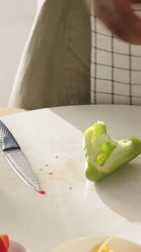 Vertical video: Holding pepper half aproned cook cleaning seeds slicing with knife on board to cook