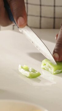 Vertical video: Hand entering with blue knife, cook dicing green bell pepper for cooking on board