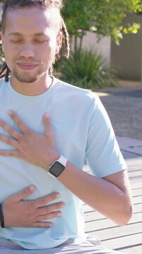 Vertical video: Breathing man in sun taking slow chest-belly breaths on deck, opening eyes smiling