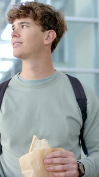 Vertical video: Scanning man checking phone for train times at station, holding sandwich