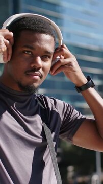 Vertical video: Adult commuter putting on white headphones in plaza, in gray tee, preparing to walk