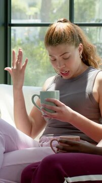 Vertical video: Leading conversation, woman in tank top gesturing and holding mug by gridded window
