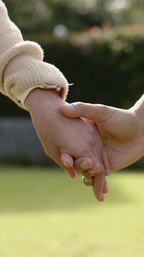Vertical video: Reaching adult hands linking and walking on lawn, showing watch, white sweater