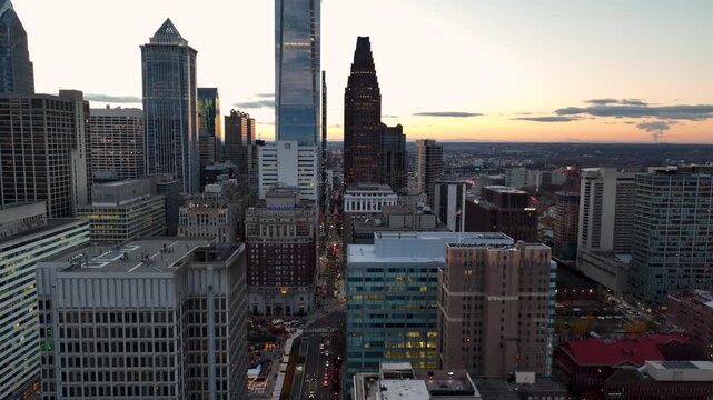 Aerial drone shot of Philadelphia downtown skyline at sunset featuring tall skyscrapers and city traffic.