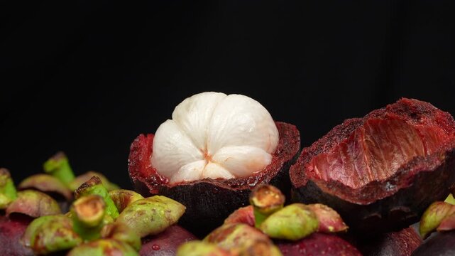 Macro loop video of an opened purple mangosteen fruit rotating against a solid black backdrop.
