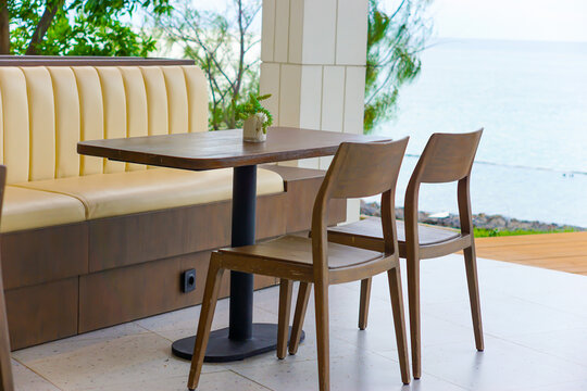 Modern outdoor cafe dining setup featuring a wooden table, chairs, and a cream booth seating next to the ocean.