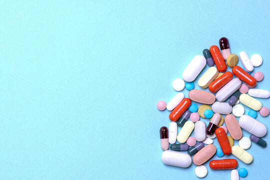 Top view of a pile of various medications on a blue surface; concept of healthcare, pharmacy, and medical treatment.