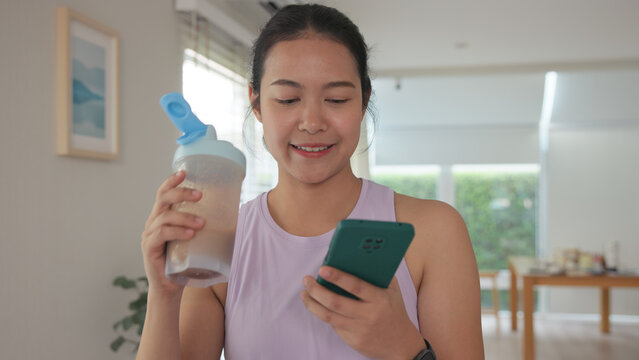 Young gen z active woman drink whey creatine shake bottle eating diet food using phone calorie plan app after home sport workout. health care asia people happy relax protect aging life weight loss.