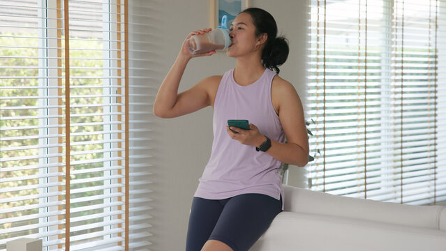 Young gen z active woman drink whey creatine shake bottle eating diet food using phone calorie plan app after home sport workout. health care asia people happy relax protect aging life weight loss.