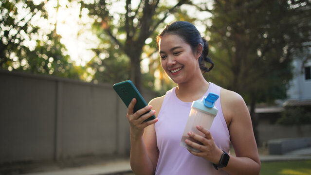 Young active woman drink whey protein shake bottle eating diet food using phone calorie AI plan app after workout health care asia people happy relax anti aging life weight loss public green park walk