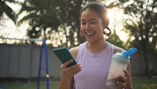 Young active woman drink whey protein shake bottle eating diet food using phone calorie AI plan app after workout health care asia people happy relax anti aging life weight loss public green park walk