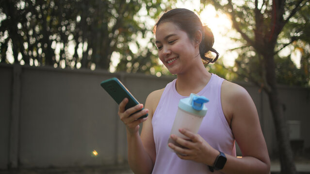 Young active woman drink whey protein shake bottle eating diet food using phone calorie AI plan app after workout health care asia people happy relax anti aging life weight loss public green park walk