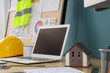 Fototapeta premium Modern architect's workplace with laptop, house model and blueprint, closeup