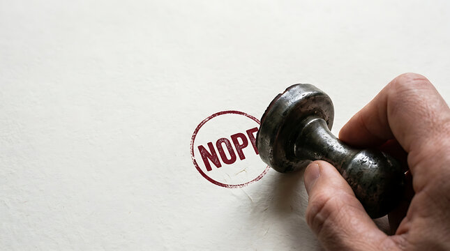 Hand holding a rubber stamp with a red nope mark on white paper