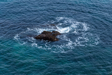 Obraz premium Ocean waves swirling around a dark solitary reef stone