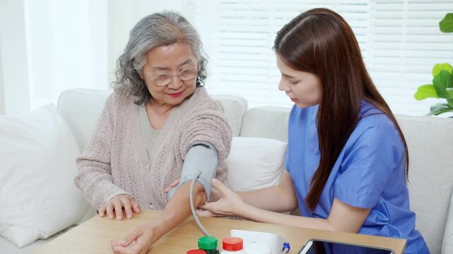 Asian woman nurse measuring blood pressure senior patient, medical checking for hypertension monitoring, caregiver support elderly woman with arterial blood pressure device, routine health checkup.