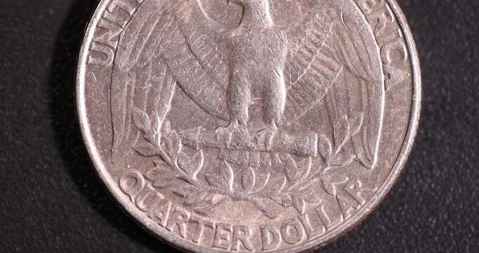 one American quarter dollar coin on a black plastic surface during rotation around its axis, an old worn American 25 cent coin during its rotation 