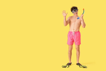 Handsome young happy man with snorkeling mask and flippers on yellow background © Pixel-Shot