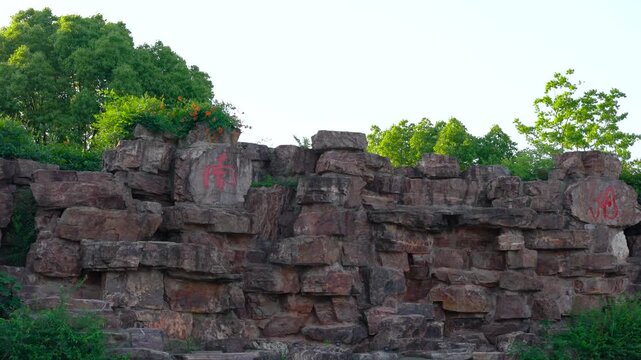 Rocky garden wall with engraved Chinese character and green trees in China