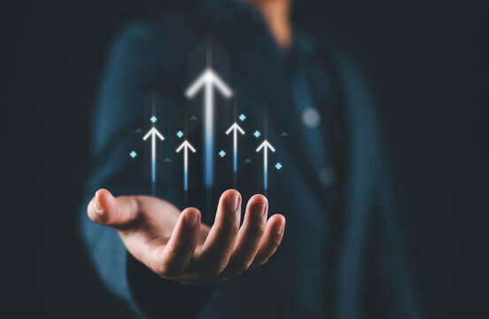 Hand holding upward arrow and target icon, representing business growth strategy, profit increase, investment success, economic development, goal achievement, and performance improvement.