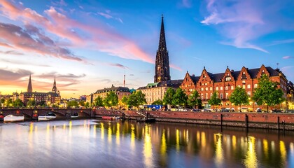 Fototapeta premium Cityscape at sunset River reflects light from buildings under a colorful sky with clouds and a tall spire