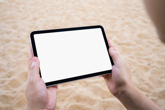 Hand holding tablet with blank screen at the beach for travel, summer vacation and digital technology concept.